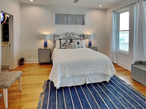 A bedroom with a bed, two bedside tables, a bench, a window, and a view of the outside.