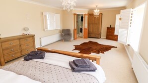 A bedroom with a large bed, a wooden dresser, a chair, a chandelier, and a cowhide rug.