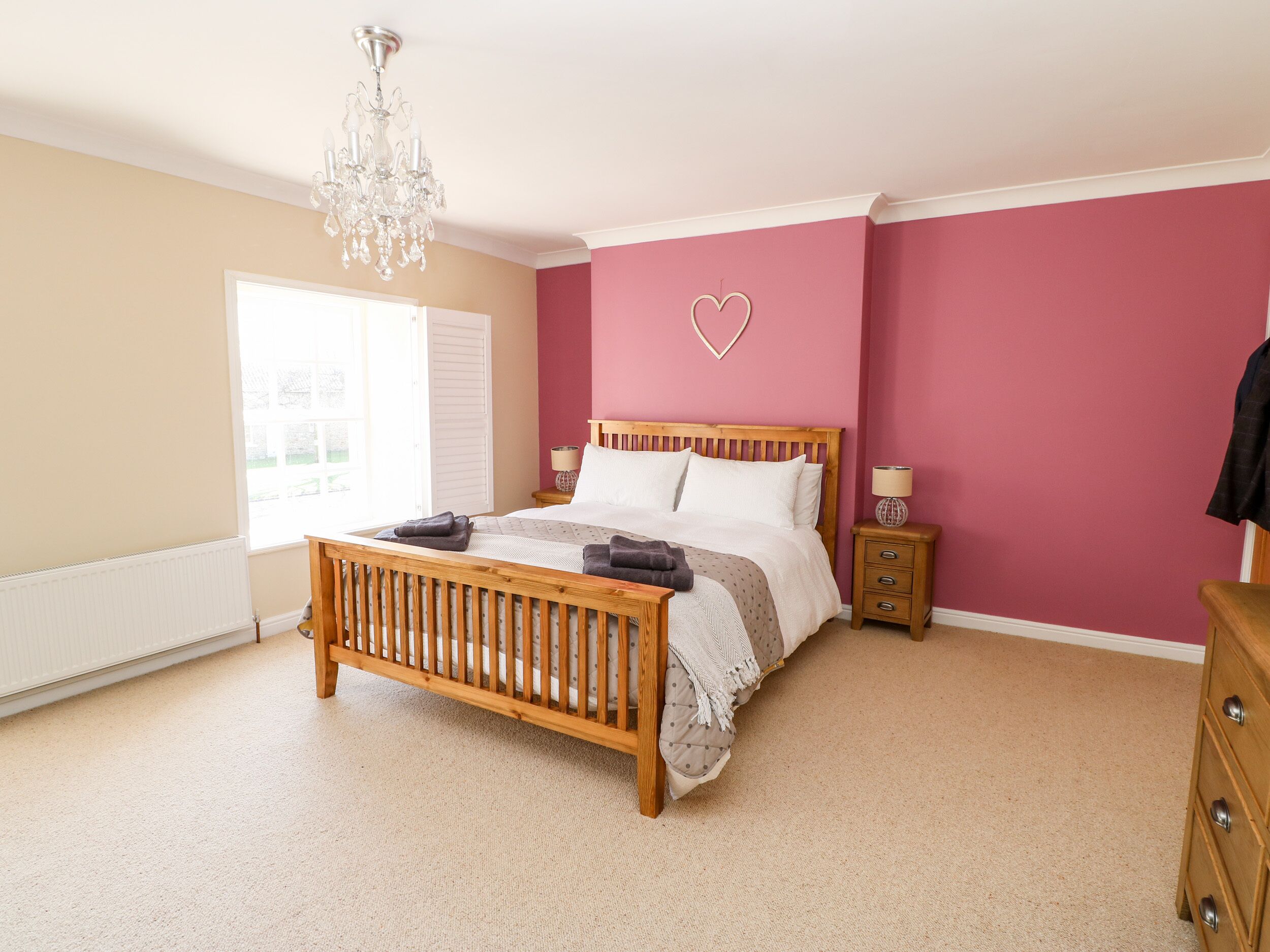 Un dormitorio con una cama de madera, una araña, un aparador y una decoración en forma de corazón.