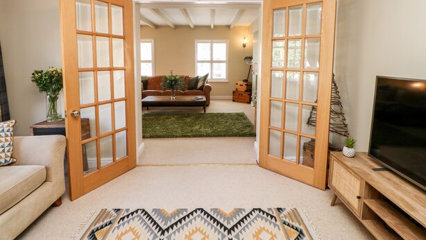 A living room with a sofa, coffee table, and TV stand. There are two wooden doors with glass panels leading to another room.