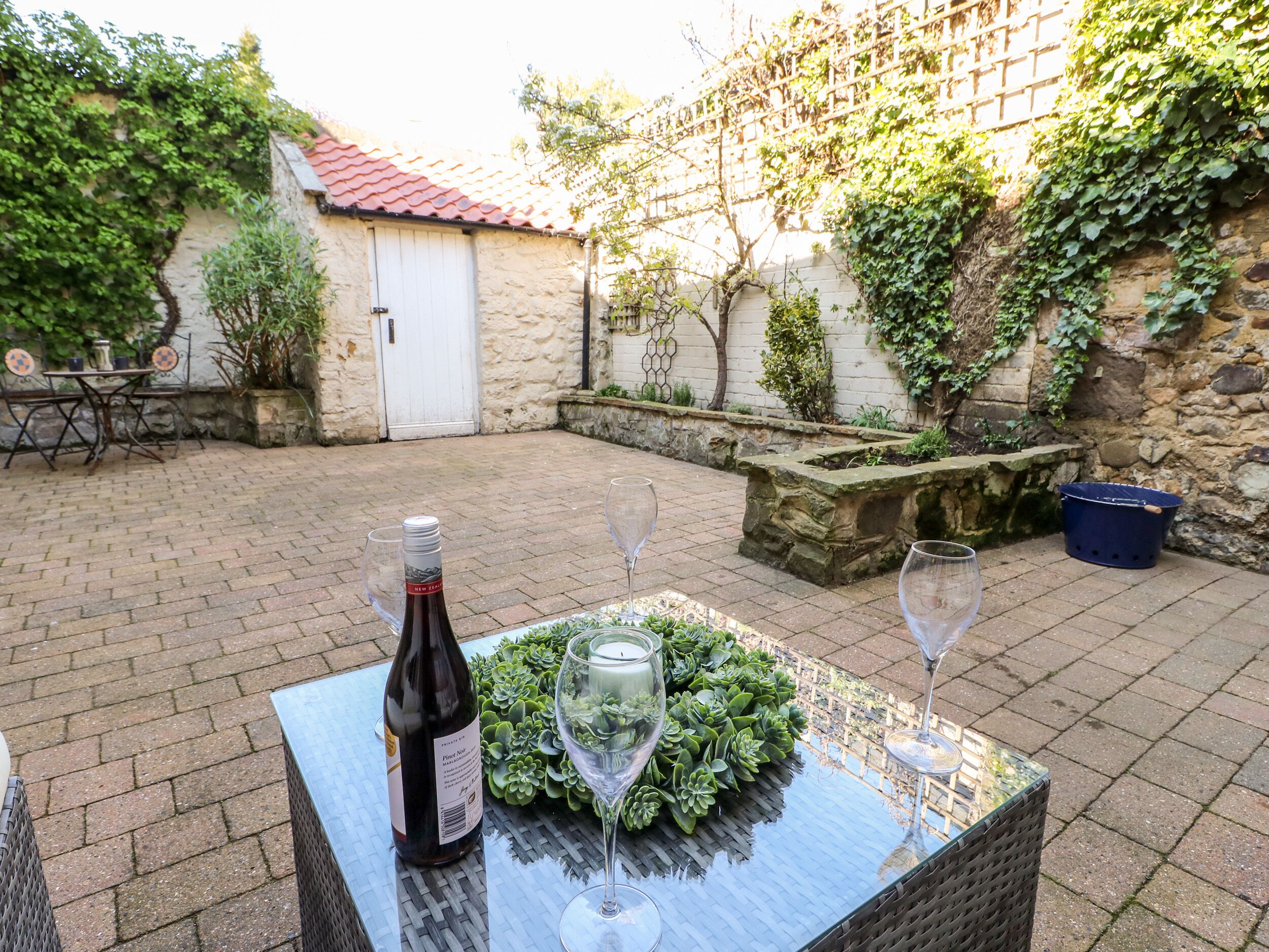 A patio with a table set for two, featuring a bottle of wine and two glasses.