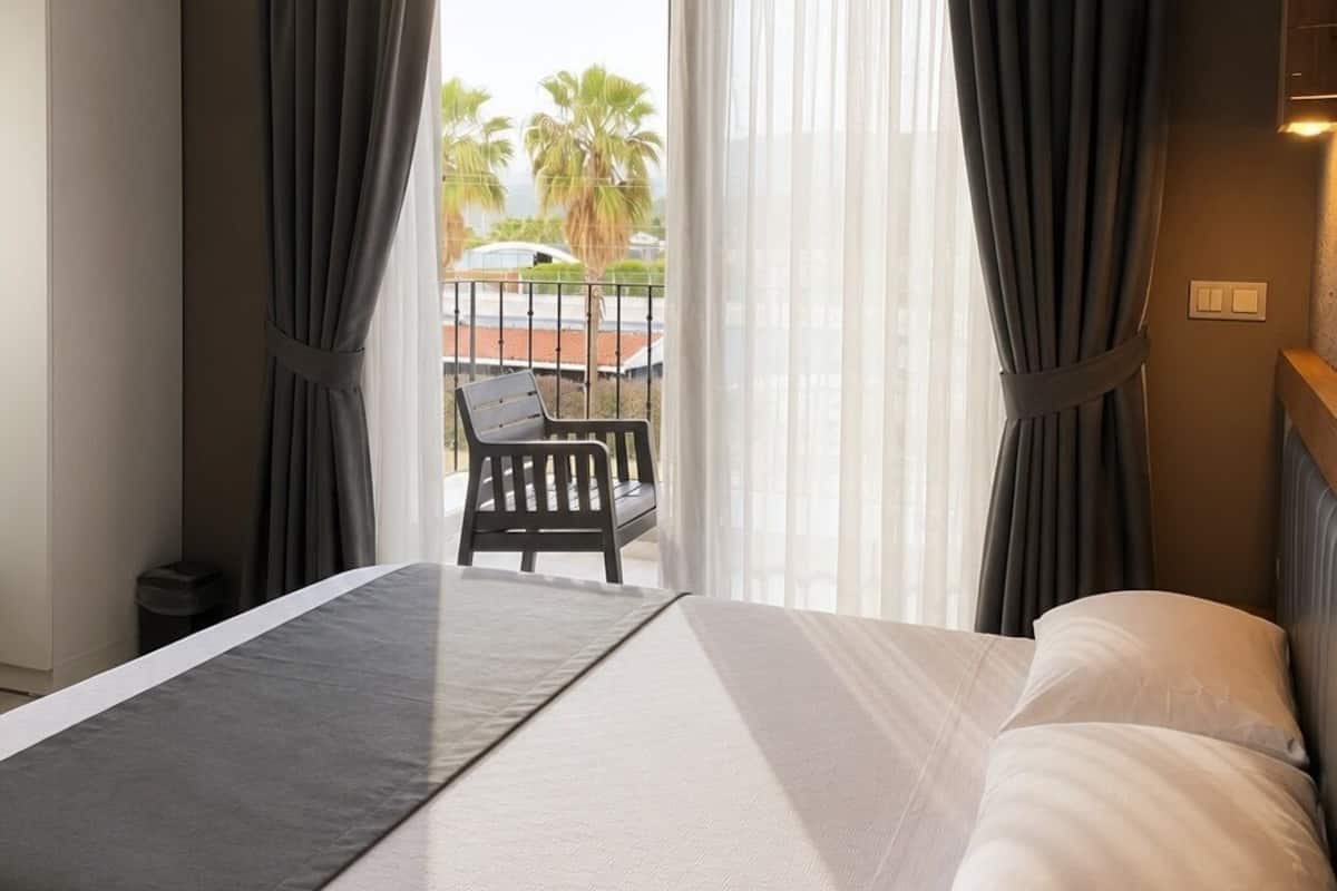 A hotel room with a bed, a chair, a view of palm trees, and a balcony.