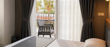 Una camera d'albergo con un letto, una sedia, vista su palme e un balcone.