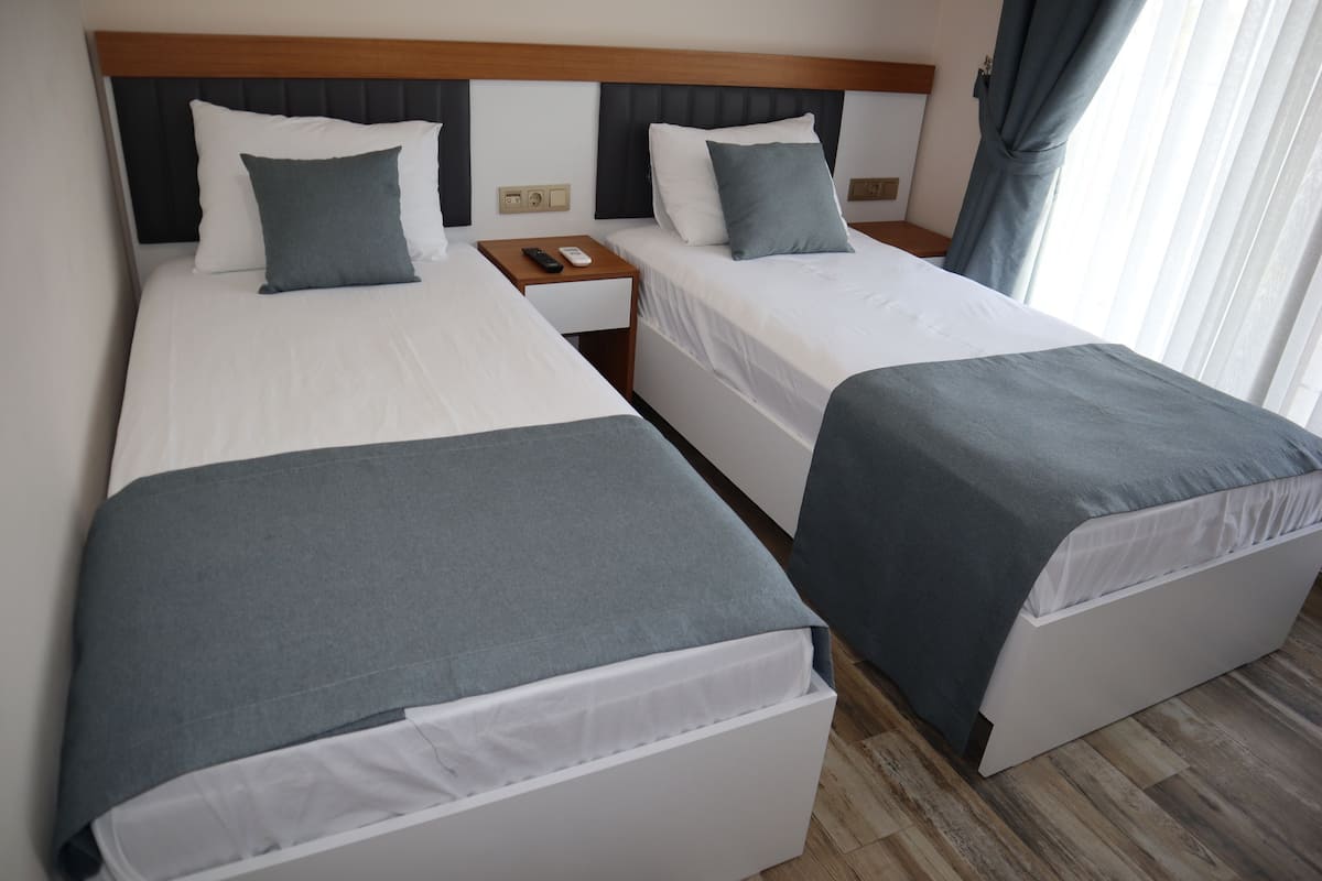 A hotel room with two beds, a wooden headboard, a nightstand with a remote control, and a window with curtains.