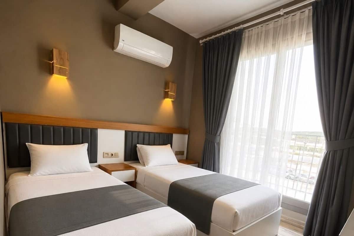 A hotel room with two beds, a wooden headboard, an air conditioning unit, a nightstand, and a large window with curtains.