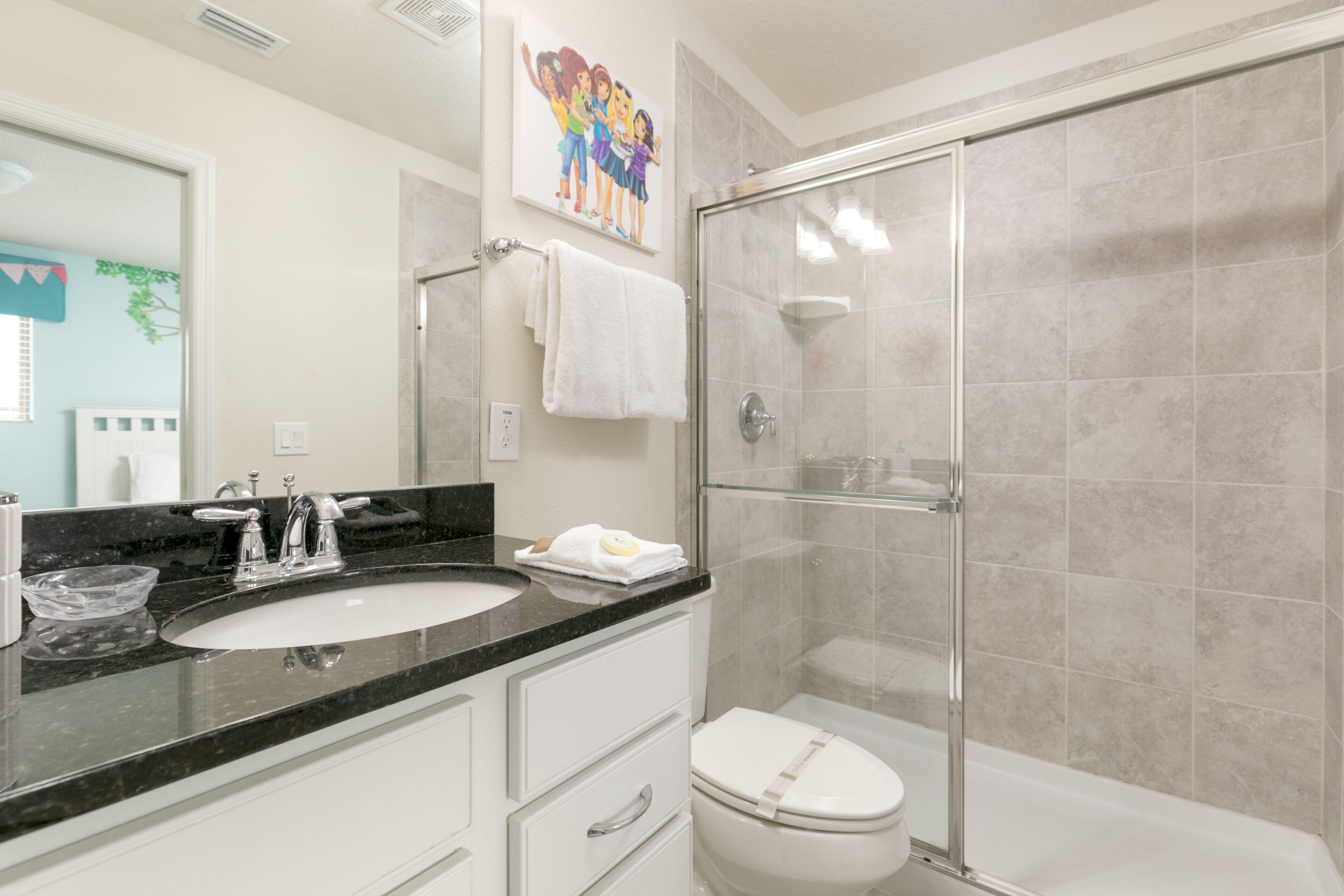 Une salle de bain avec un lavabo à vasque et un plan de toilette noir, des toilettes blanches et une douche à paroi de verre.