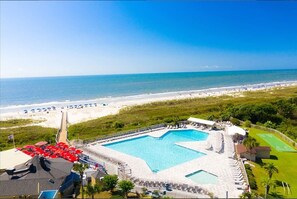 Relax by the star-shaped pool surrounded by lounge chairs and umbrellas, with access to the beach and a scenic ocean view.