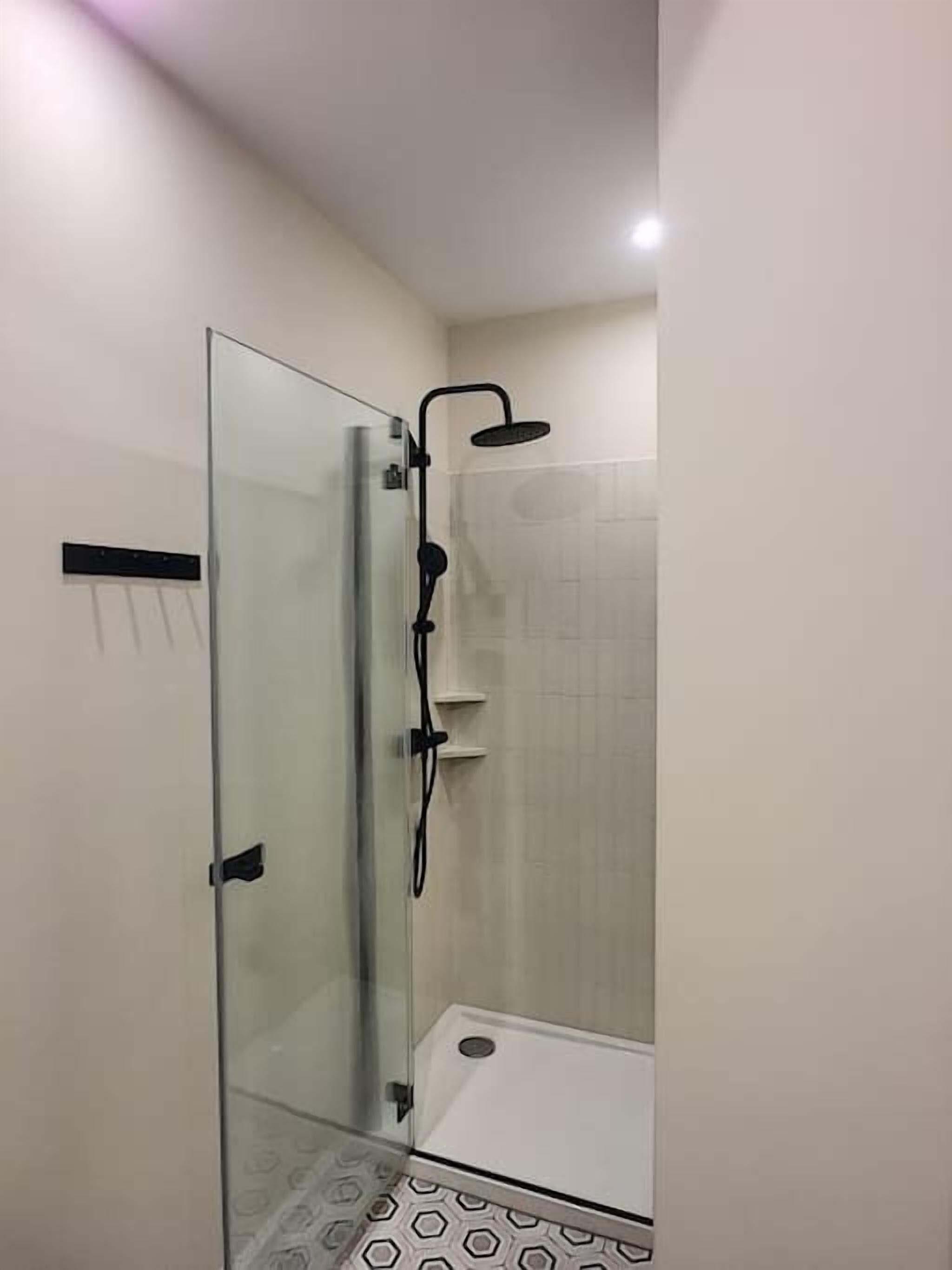 A glass-enclosed shower with a handheld showerhead and a wall-mounted control panel.