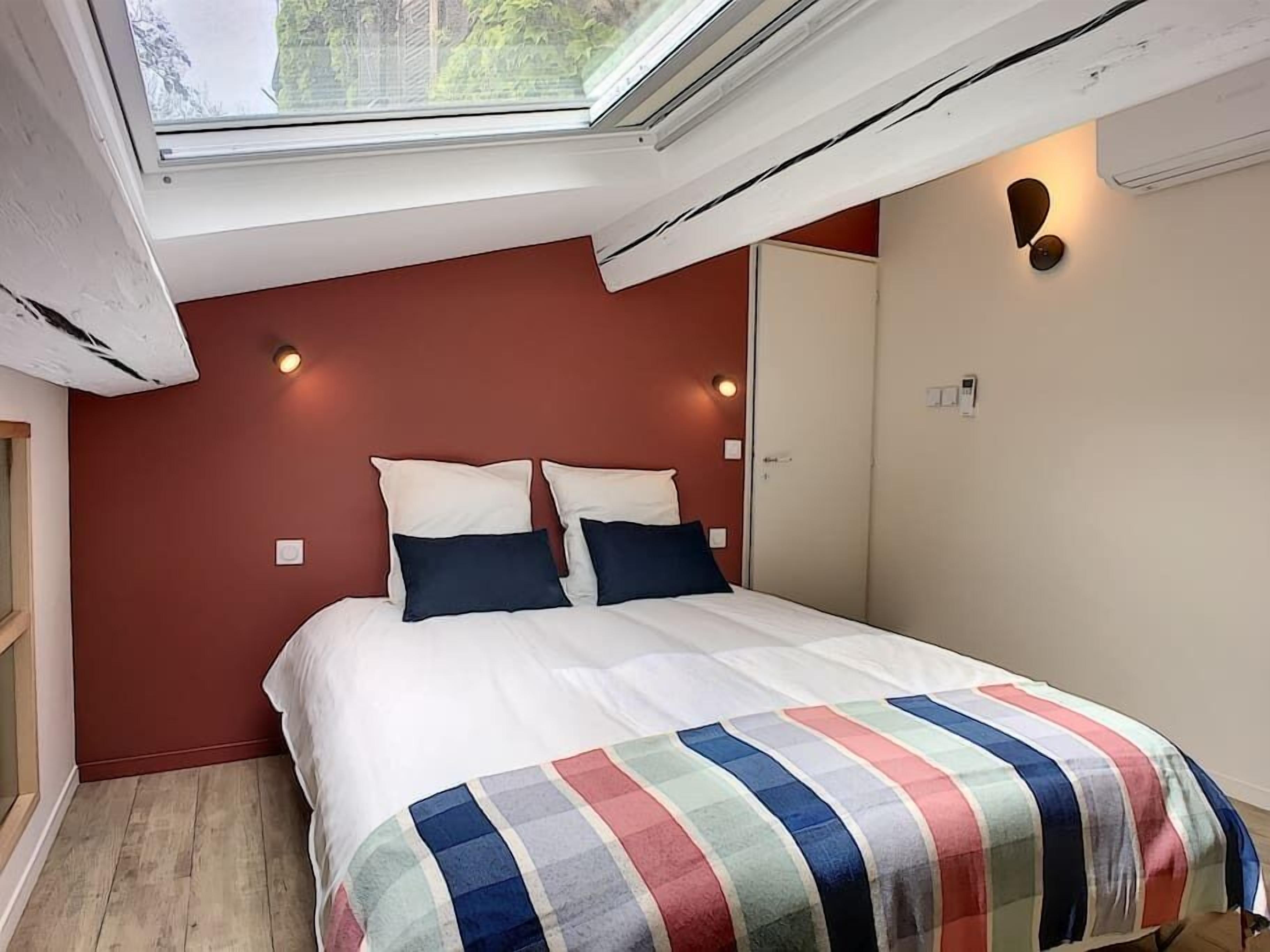 A bedroom with a skylight, a bed with a striped blanket, and a red wall.
