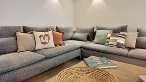 Een moderne woonkamer met een grijze modulaire bank, decoratieve kussens en een gevlochten mand op een houten salontafel.