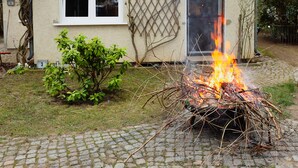 A house with a fire in the yard, a small garden, and a paved driveway. - Ferienhäuser - Pappelallee (Biesenthal)