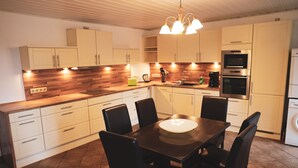 A modern kitchen with white cabinets, a wooden countertop, and a dining table with chairs. - Ferienhäuser - Pappelallee (Biesenthal)
