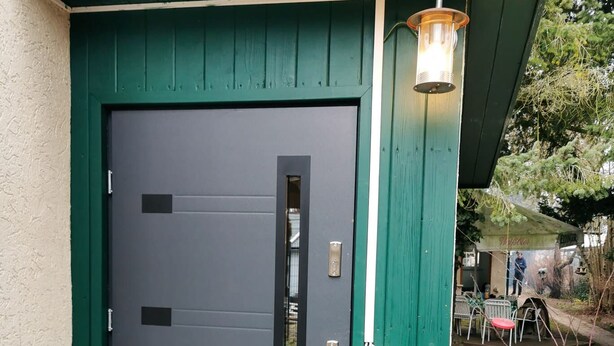A dark grey door with a vertical window, a green door frame, and a metal handle. - Ferienhäuser - Pappelallee (Biesenthal)
