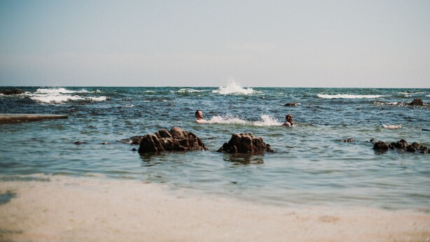 Une plage avec une eau claire, des rochers et des gens qui se baignent.