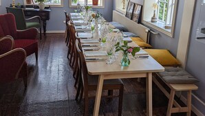 Un espace repas avec une longue table dressée pour le repas, des chaises en bois et une vue sur la mer grâce à de grandes fenêtres.