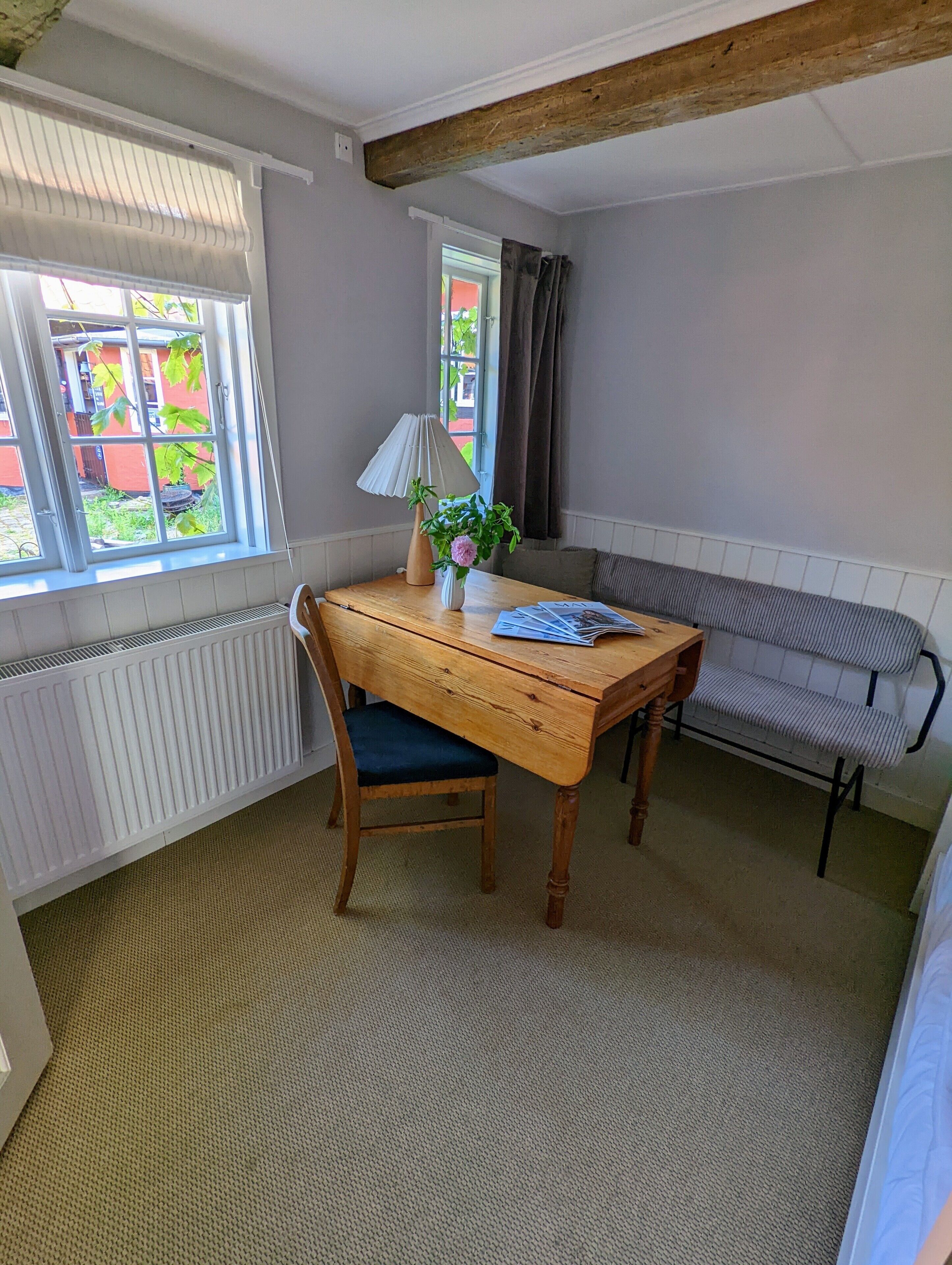 Une pièce avec une table en bois, une chaise, un radiateur, une fenêtre avec des rideaux et un banc.