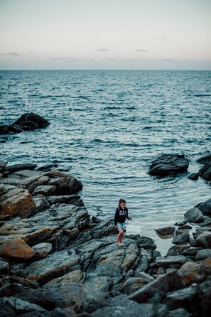 A rocky shoreline with a person standing on the rocks. - Næsgaarden Pensionat (Allinge)