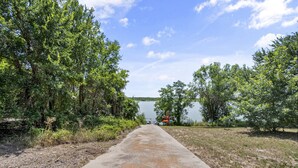 A concrete pathway leading to a body of water, surrounded by dense green foliage. - Lakefront, Kayaks, 2.5 acres, March Dates Open (Granbury)