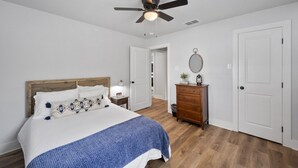 A bedroom with a bed, wooden headboard, white walls, a ceiling fan, a dresser, and a door. - Lakefront, Kayaks, 2.5 acres, March Dates Open (Granbury)