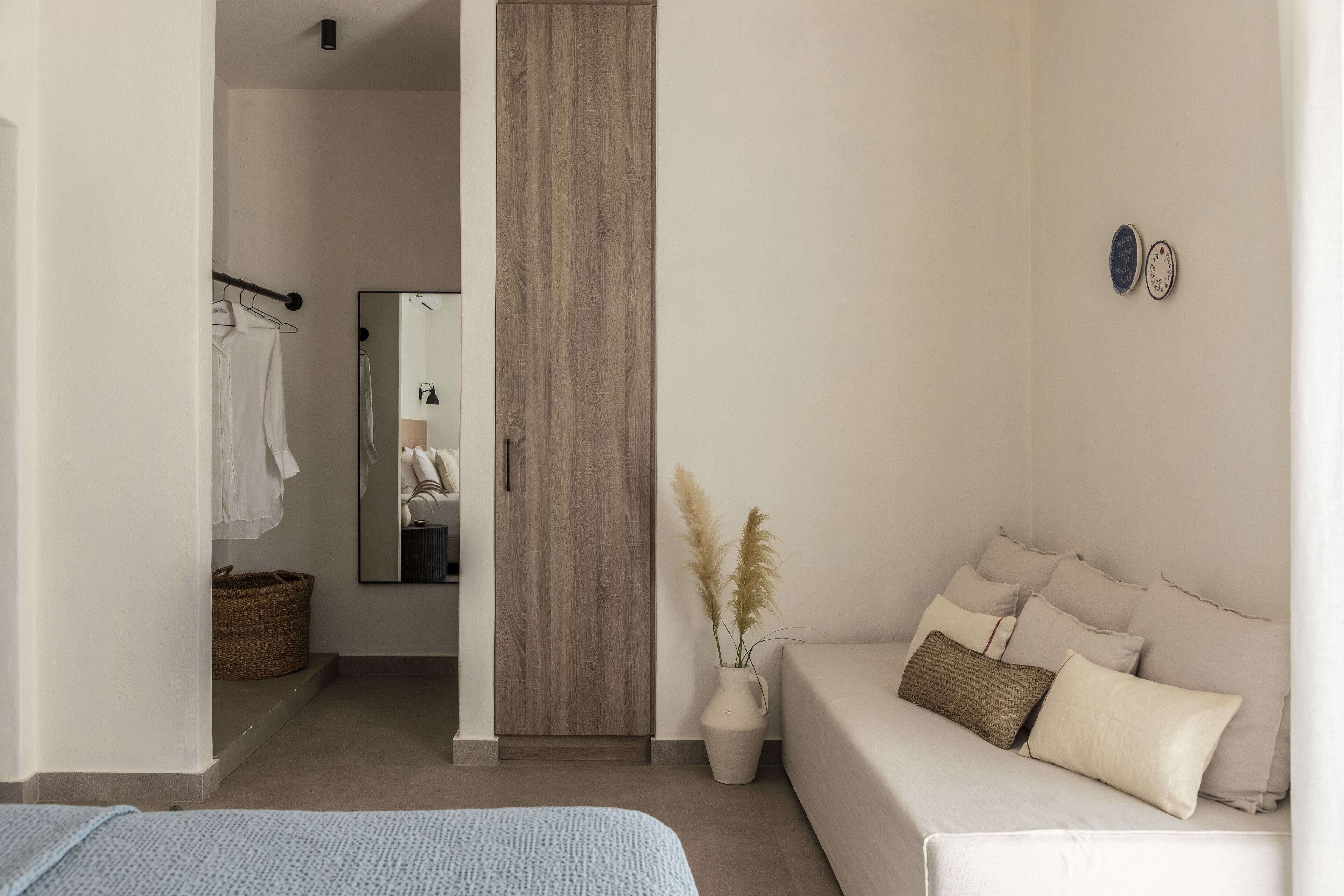 Une chambre à coucher moderne et minimaliste, avec un grand lit, une table de chevet, une armoire en bois et une petite table d’appoint sur laquelle est posé un vase contenant des plumes d’herbe des pampas.