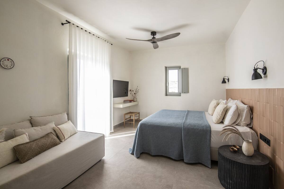 A modern bedroom with a bed, a sofa, a desk, and a television.