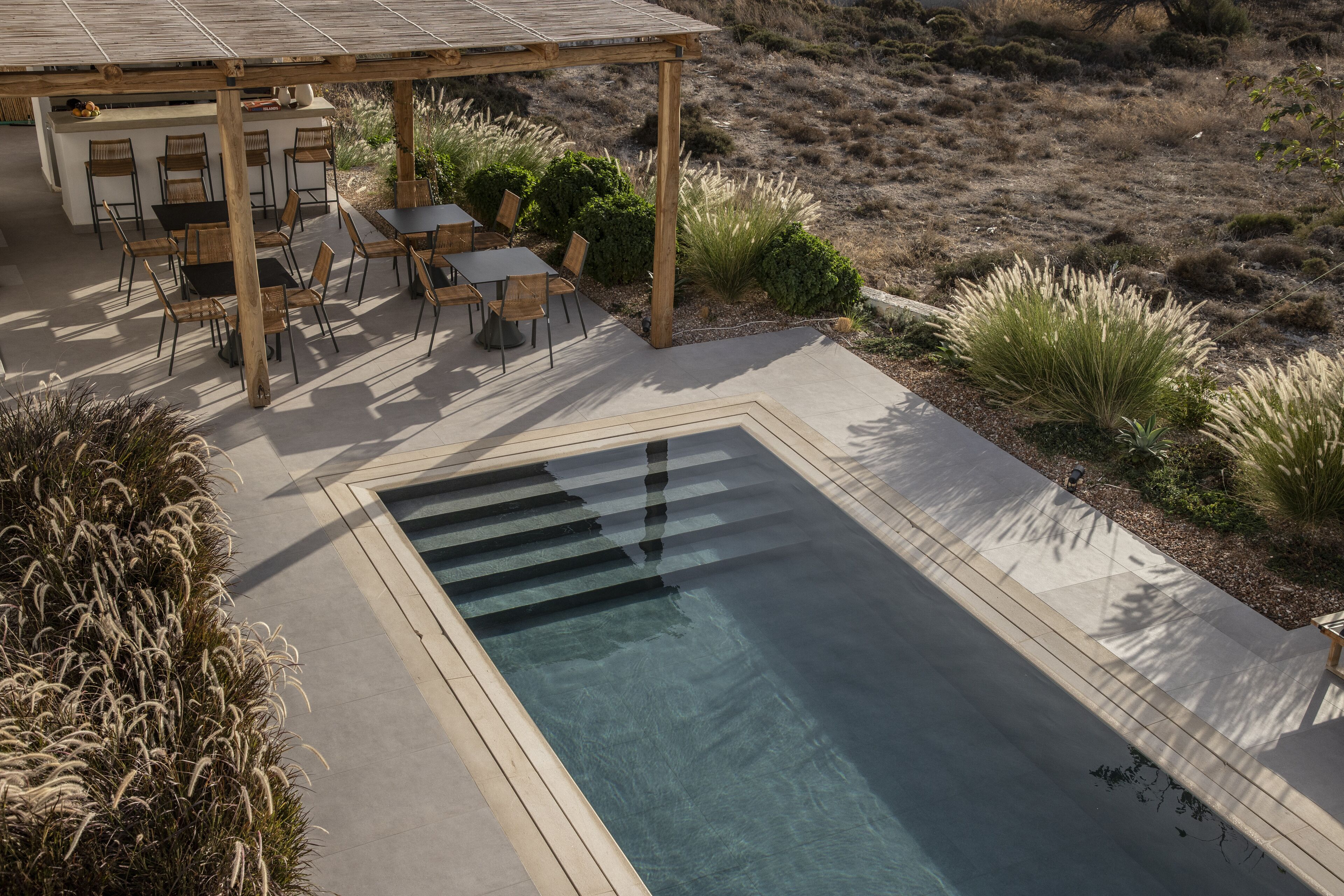A pool area with a pergola, seating, and a view of the surrounding landscape.