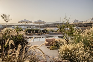 A poolside area with lounge chairs and umbrellas, surrounded by greenery. - Nysis Koufonisia (Naxos)