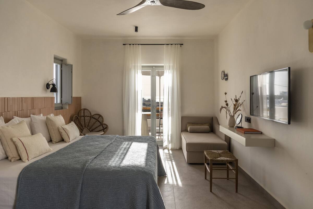 A bedroom with a bed, a desk, a chair, a TV, and a window with curtains.