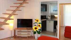 Un interior moderno con una escalera de madera, un televisor de pantalla plana, un sofá rojo y una zona de cocina.