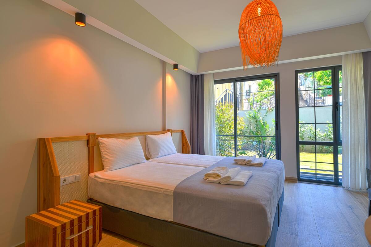 A double bed with white linens, a wooden headboard, and a small wooden side table with a drawer.