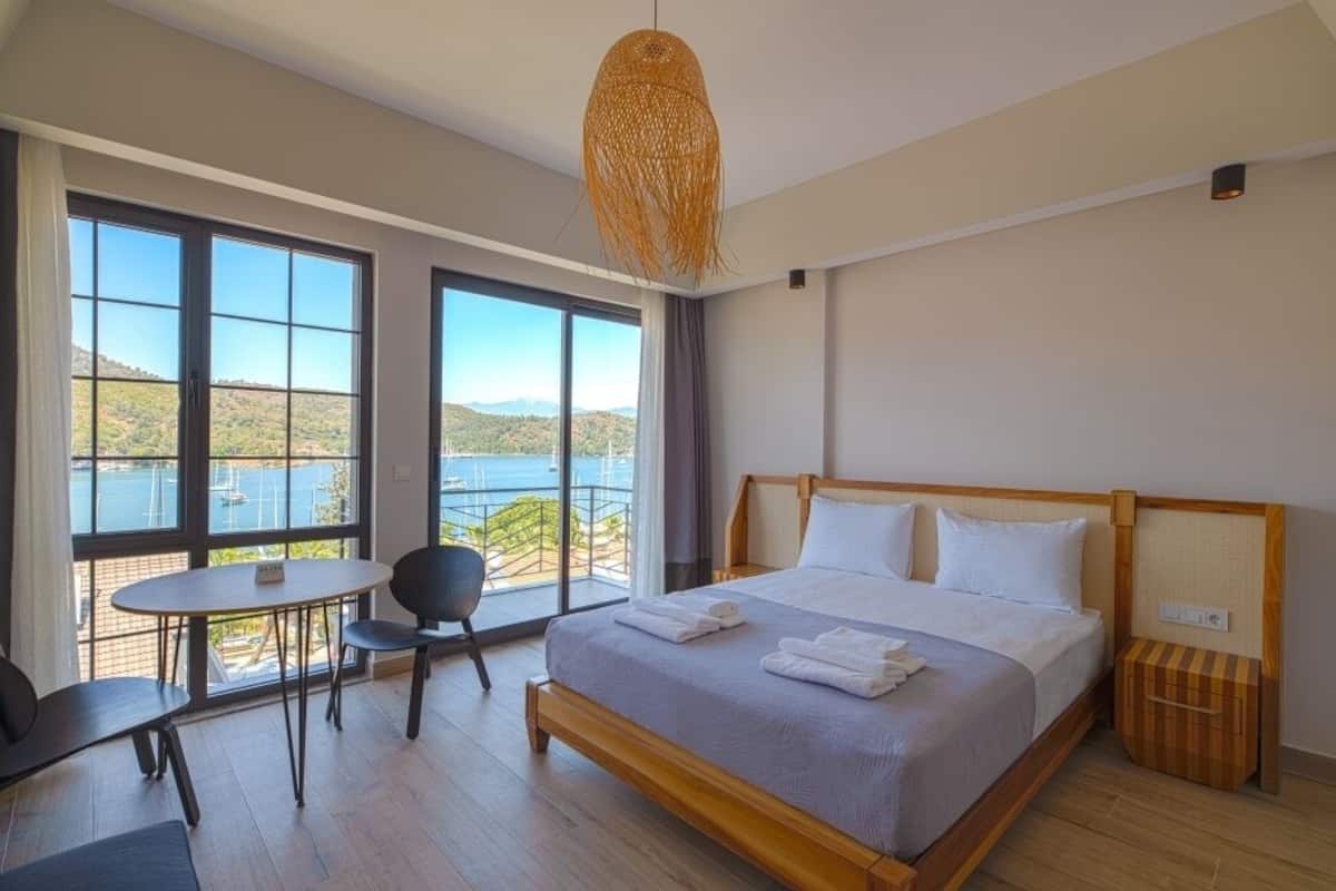 A bedroom with a large bed, a dining table, and chairs, a view of the sea, and a balcony.