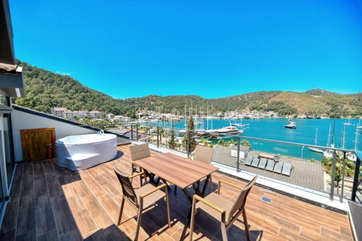 A balcony with a wooden table and chairs, a hot tub, and a view of a marina with boats.