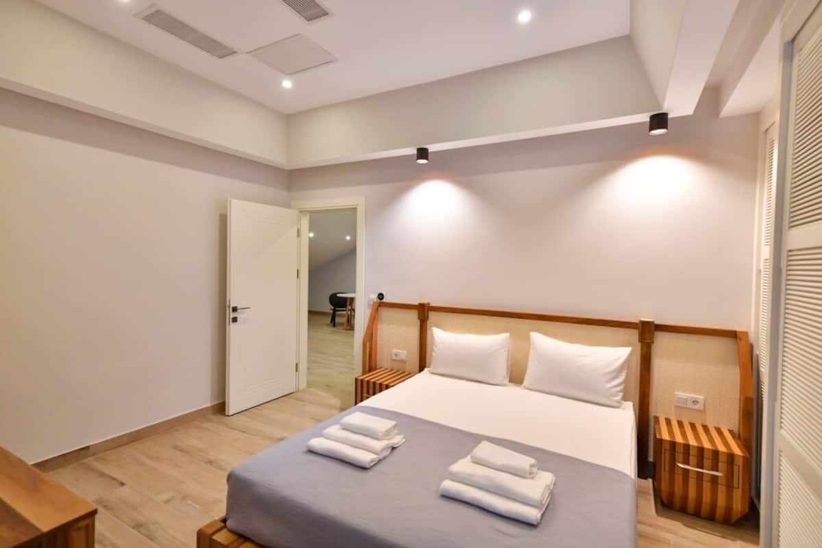 A modern hotel room with a large bed, bedside tables, and a door leading to another room.