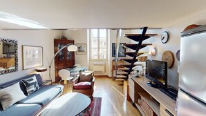 Una sala de estar acogedora con un sofá, un televisor y una escalera que sube a otro nivel.