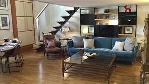 Una sala moderna con un sofá azul, una mesa de centro de madera y una escalera.