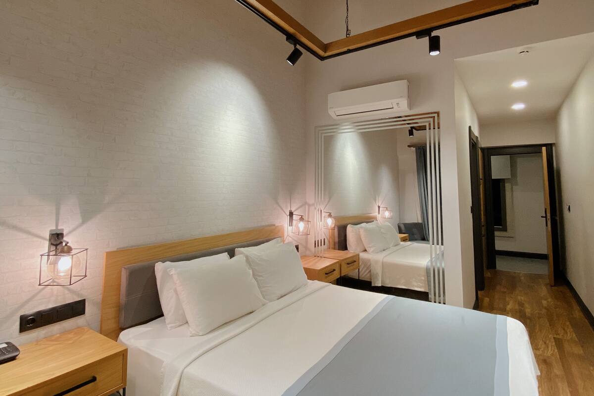 Habitación de hotel moderna con una cama grande, mesitas de noche, un espejo y un equipo de aire acondicionado.
