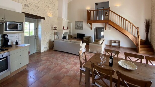 A spacious living area with a high ceiling, a wooden staircase, and a kitchen with modern appliances. - Le Genet - Ancienne grange avec piscine privé (Chalais)