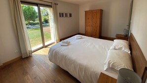 A bedroom with a large bed, wooden wardrobe, and a sliding glass door leading to a garden. - Le Genet - Ancienne grange avec piscine privé (Chalais)