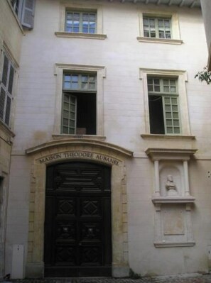 A building with a dark wooden door and a plaque reading "MAISON THÉODORE AUBANEL".