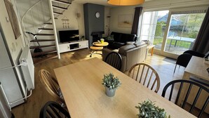 Una sala de estar moderna con una escalera, un televisor de pantalla plana, una chimenea y un comedor con sillas y una mesa.