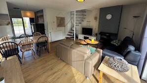 Una sala de estar moderna con sofá, mesa de comedor, sillas, una escalera y una chimenea.