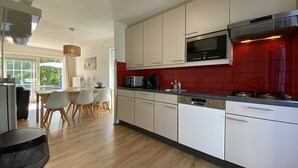 Una cocina moderna con armarios blancos, salpicadero rojo y electrodomésticos de acero inoxidable.