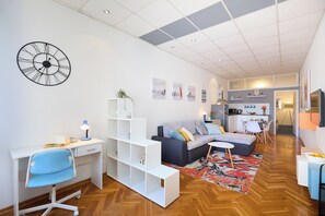 Ein modernes Wohnzimmer mit einem weißen Schreibtisch, einem blauen Sessel, einem grauen Sofa und einem gemusterten Teppich.