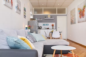 A modern living room with a grey sofa, a small white table, and a kitchen in the background.