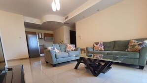 A modern living room with a sofa and a glass coffee table, a kitchen area with a refrigerator and microwave, and a dining area with chairs. - Abdoun Panorama (Amman)