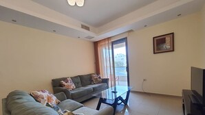 A living room with a sofa, a glass coffee table, a TV, and a window with curtains. - Abdoun Panorama (Amman)