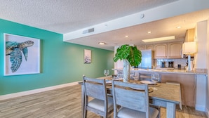 A dining area with a wooden table and chairs, a large plant, and artwork on the walls. - DIRECT BEACHFRONT! SWIMMING POOL! (Indian Shores)