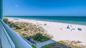 A beach with white sand, clear blue water, and a few people. There are blue beach umbrellas and lounge chairs. - DIRECT BEACHFRONT! SWIMMING POOL! (Indian Shores)