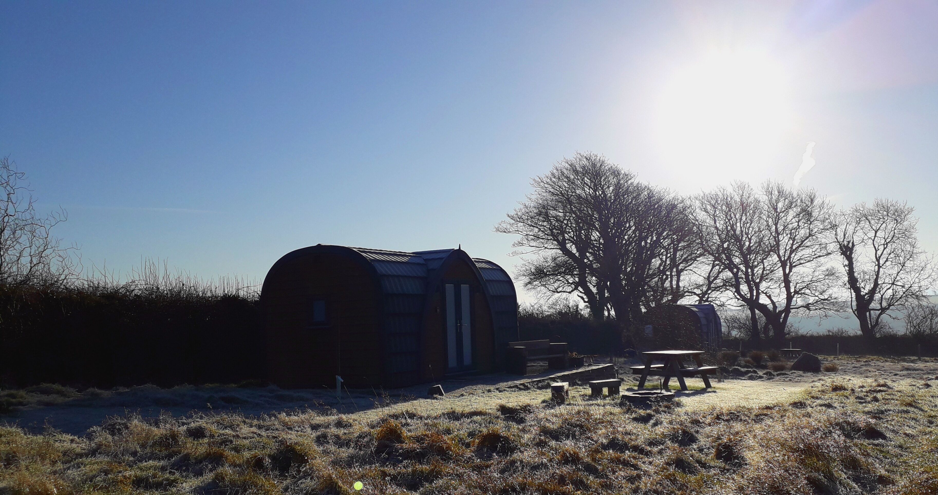 A rustic outdoor setting with a wooden structure, possibly a barn, and picnic tables in a field.