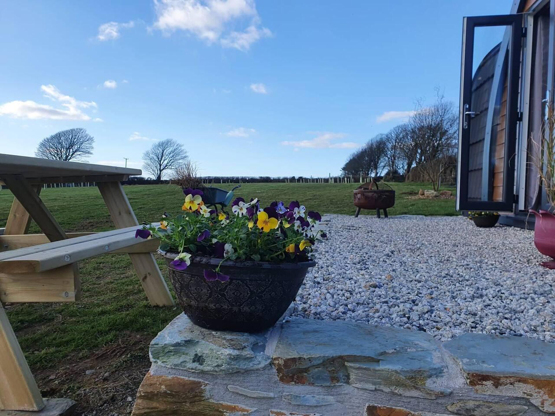 Un banc en pierre avec un pot de fleurs devant une table de pique-nique en bois.